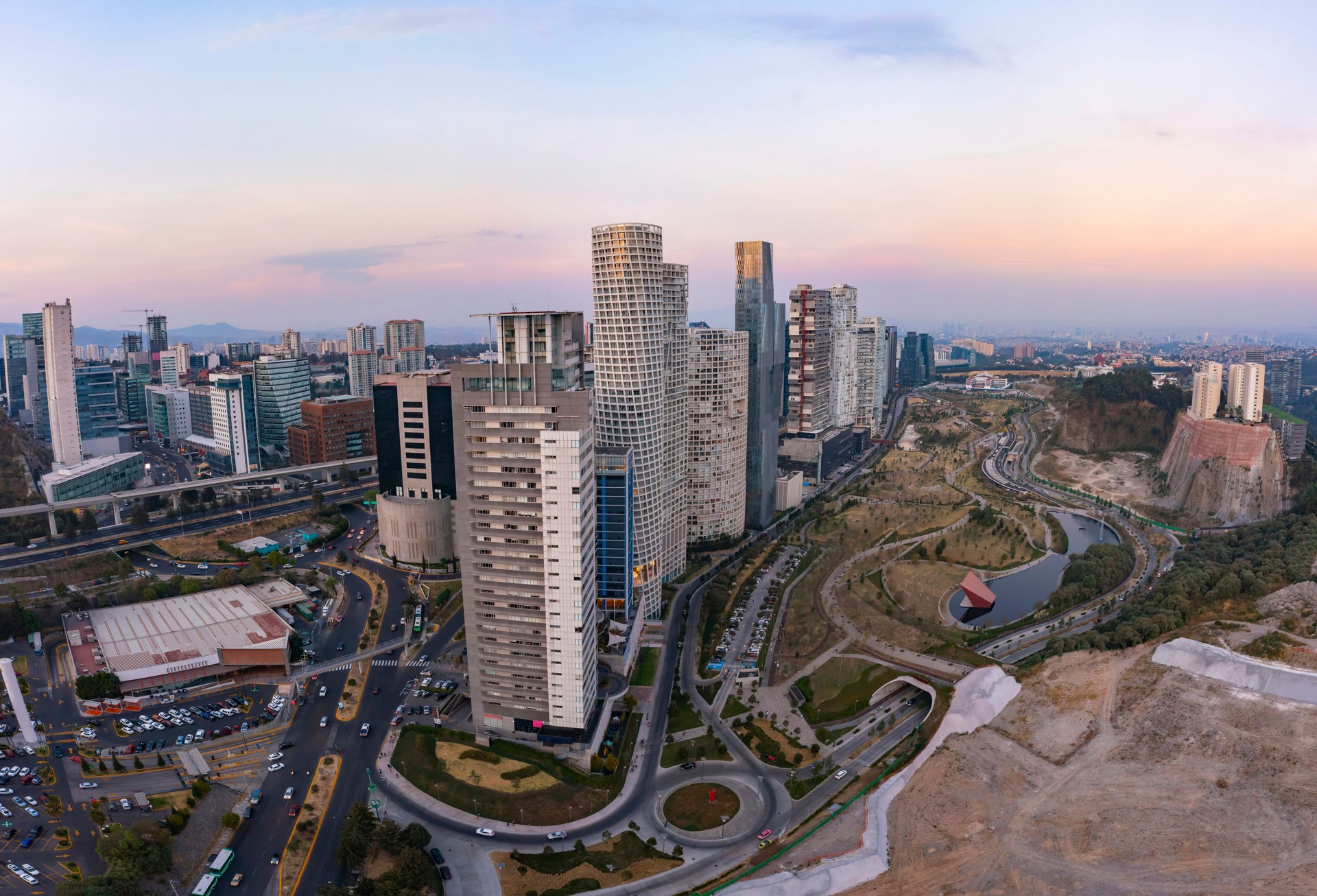 Recorrido aéreo sobre la zona financiera de Santa Fe repleta de rascacielos de departamentos y oficinas junto al parque La Mexicana con un hermoso atardecer de fondo